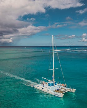 A catamaran sails in clear blue waters under a partly cloudy sky, ideal for a tranquil vacation vibe.